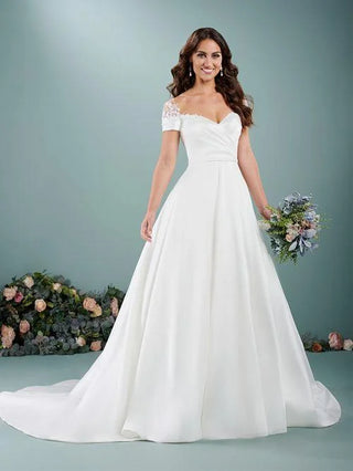 Woman in a white wedding dress holding a bouquet against a gray background with floral decorations.