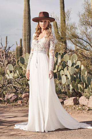 Woman in a white lace dress and brown hat standing in a desert landscape with cacti.