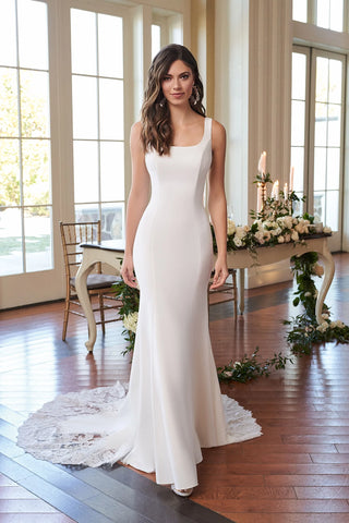Woman in a white wedding dress standing in a decorated room with large windows.